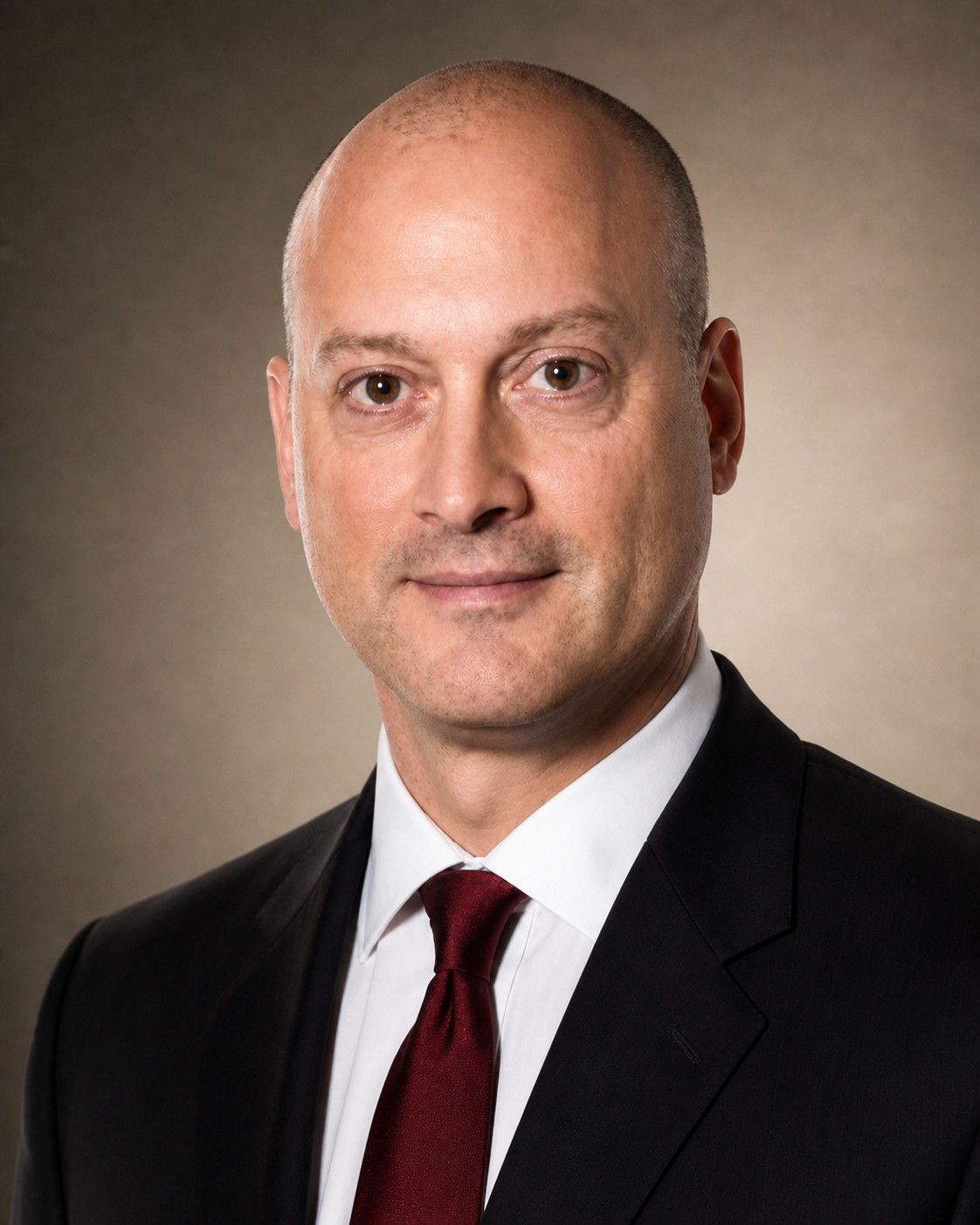 Peter DeCaprio in a formal studio portrait wearing a dark suit, white shirt and burgundy tie